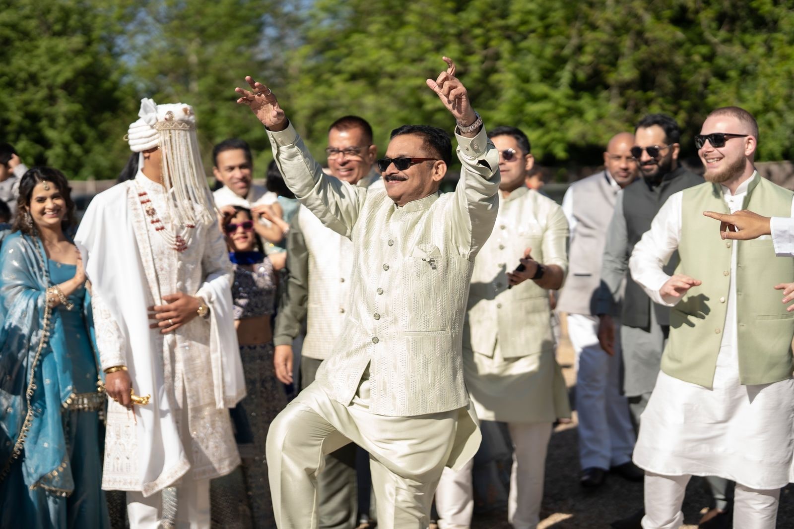 Guests dancing in the baraat as the groom arrives in a cream sherwani and sehra